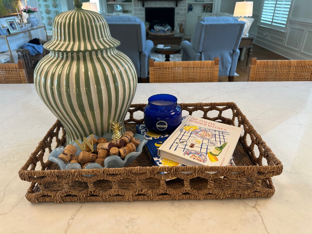 Large kitchen island styled with a woven tray, green striped vase, cookbooks, candle and bowl of wine corks